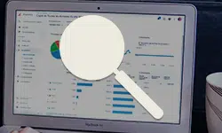 Laptop screen showing a data analytics dashboard with charts and lists, overlaid by a white magnifying glass suggesting data search/analysis.
