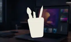White cup with two pens in front of a blurred desk and laptop background